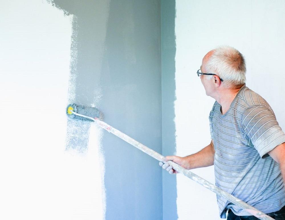 An Elderly Man Paints a Wall with a Roller