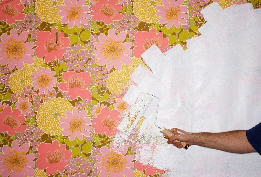 Man painting over floral wallpaper